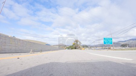 Photo for On a crisp winter day, a car cruises along the iconic Highway 101 near San Luis Obispo, California. The surrounding landscape is brownish and subdued, with rolling hills and patches of coastal - Royalty Free Image