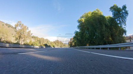 Foto de En un día de invierno crujiente, un automóvil cruza a lo largo de la icónica autopista 1 cerca de San Luis Obispo, California. El paisaje circundante es marrón y tenue, con colinas onduladas y parches de costa - Imagen libre de derechos