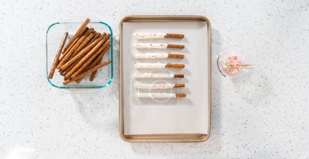 Flat lay. Homemade candy cane chocolate-covered pretzel rods are drying on a baking sheet lined with parchment paper.