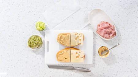 Foto de Acostado. Montaje de sándwiches de jamón, pepino y brote en la tabla de cortar blanca. - Imagen libre de derechos