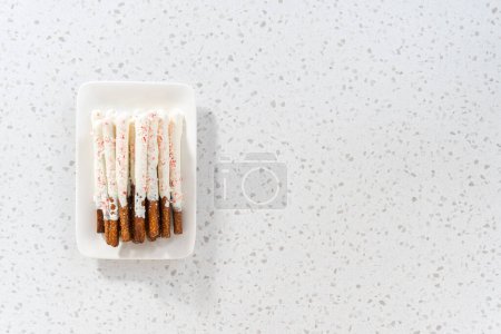 Photo for Flat lay. Pile of homemade candy cane chocolate-covered pretzel rods on a white serving plate. - Royalty Free Image