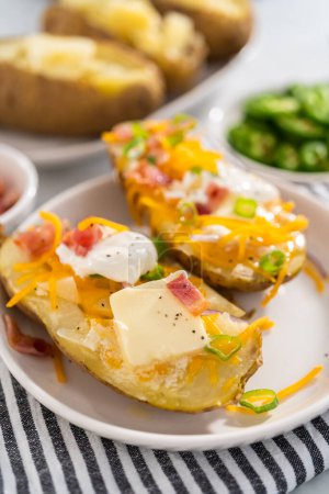 Foto de Pressure Cooker Baked Potatoes. Garnished large baked potatoes with butter, sour cream, cheese, and bacon bits on a white plate. - Imagen libre de derechos
