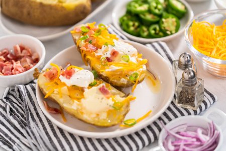 Photo for Pressure Cooker Baked Potatoes. Garnished large baked potatoes with butter, sour cream, cheese, and bacon bits on a white plate. - Royalty Free Image