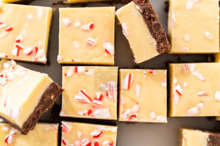 Photo for Cutting candy cane fudge with a large kitchen knife into square pieces on a white cutting board. - Royalty Free Image