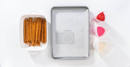 Téléchargez les photos : Pose plate. Tremper les tiges de bretzels dans une tasse en silicone avec du chocolat fondu pour faire des tiges de bretzels recouvertes de chocolat pour la Saint-Valentin. - en image libre de droit