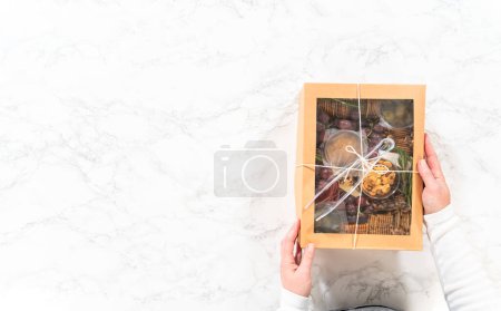 Foto de Acostado. Caja de charcutería con carne en rodajas, queso, galletas y uvas, todo perfectamente empaquetado en una caja de regalo marrón. - Imagen libre de derechos