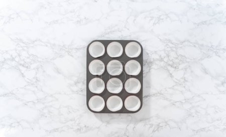 Photo for Flat lay. Lining cupcake pan with foil cupcake liners to bake red velvet cupcakes with white chocolate ganache frosting. - Royalty Free Image