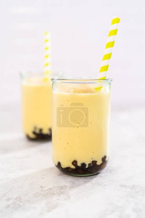 Téléchargez les photos : Freshly made mango boba smoothie in a drinking glass with a paper straw. - en image libre de droit