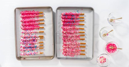Flat lay. Drizzling melted chocolate over chocolate-dipped pretzels rods and decorating with sprinkles to make chocolate-covered pretzel rods for Valentines Day.