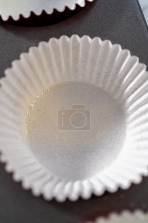 Photo for Lining cupcake pan with foil cupcake liners to bake red velvet cupcakes with white chocolate ganache frosting. - Royalty Free Image