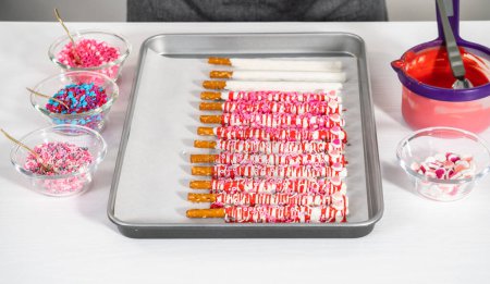 Drizzling melted chocolate over chocolate-dipped pretzels rods and decorating with sprinkles to make chocolate-covered pretzel rods for Valentines Day.
