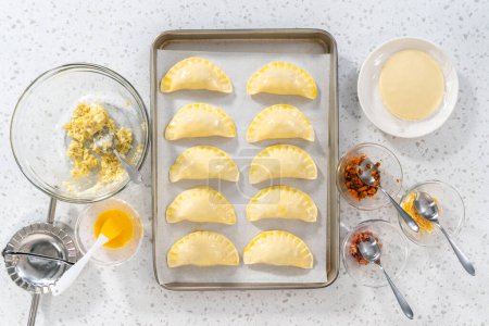 Téléchargez les photos : Pose plate. Brosser les empanadas de petit déjeuner non cuites avec des œufs et des patates douces avec le lavage des œufs. - en image libre de droit
