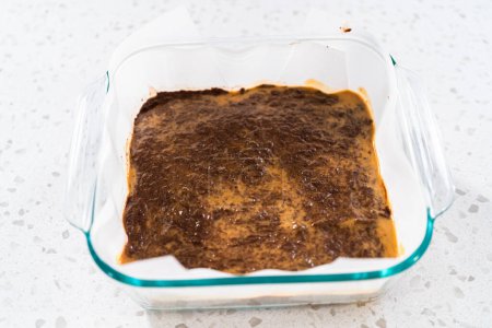 Téléchargez les photos : Verser le mélange de caramel dans le moule tapissé de papier sulfurisé pour préparer le caramel au beurre d'arachide au chocolat. - en image libre de droit