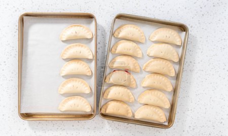 Téléchargez les photos : Flay lay. Empanadas de cerises douces non cuites sur une plaque à pâtisserie tapissée d'une plaque à pâtisserie en papier parchemin. - en image libre de droit
