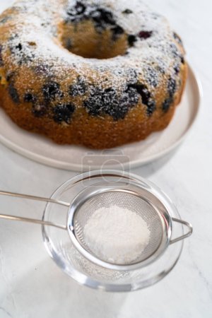 Photo for Dusting freshly baked lemon blueberry bundt cake with powdered sugar. - Royalty Free Image