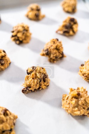 Photo for Scooping cookie dough with dough scoop into a baking sheet lined with parchment paper to bake soft oatmeal raisin walnut cookies. - Royalty Free Image