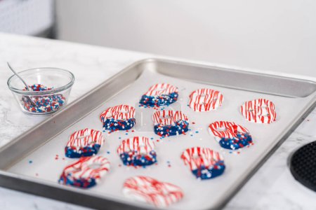 Photo for Dipping pretzels twists into melted chocolate to make red, white, and blue chocolate-covered pretzel twists. - Royalty Free Image