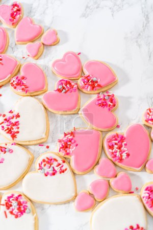 Photo for Decorating heart-shaped sugar cookies with pink and white royal icing for Valentines Day. - Royalty Free Image
