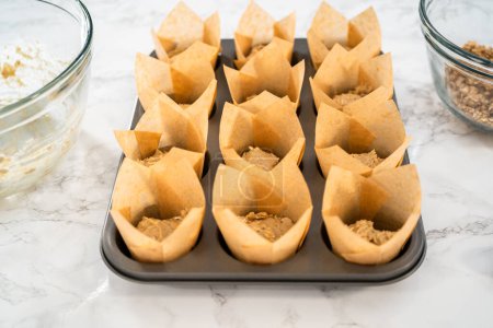Téléchargez les photos : Ramasser la pâte avec une cuillère à pâtisserie dans une casserole à cupcake doublée de doublures de muffins en papier tulipe pour cuire des muffins à l'avoine banane. - en image libre de droit