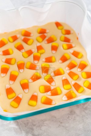 Photo for Pouring fudge mixture into the square glass baking pan lined with parchment paper to prepare candy corn fudge. - Royalty Free Image
