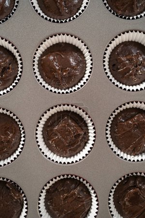 Téléchargez les photos : Scooping pâte à gâteau avec cuillère à pâte dans des doublures de papier d'aluminium cupcake pour cuire des cupcakes à la menthe poivrée au chocolat. - en image libre de droit