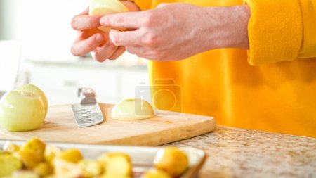 Photo for In the welcoming setting of a modern kitchen, a young man continues his dinner preparation process. Hes currently involved in slicing yellow onions into rings, prepping them for grilling on an - Royalty Free Image