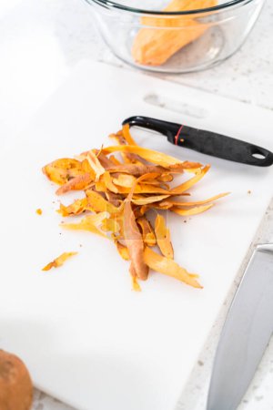 Téléchargez les photos : Peler les patates douces avec un éplucheur de pommes de terre pour faire des patates douces rôties au four. - en image libre de droit