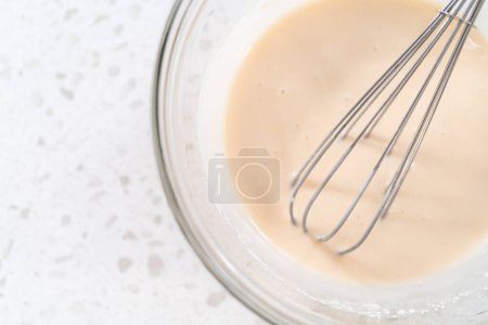 Téléchargez les photos : Mélanger les ingrédients avec un fouet à la main dans un bol à mélanger en verre pour faire le glaçage à la vanille. - en image libre de droit