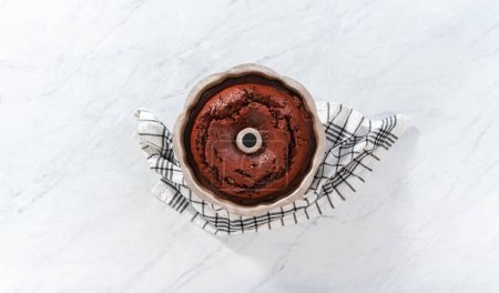 Téléchargez les photos : Pose plate. Refroidissement gâteau bundt en velours rouge fraîchement cuit sur un comptoir de cuisine. - en image libre de droit