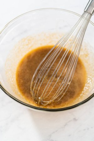 Téléchargez les photos : Mélanger les ingrédients humides dans un grand bol de mélange en verre pour cuire les noix de macadamia au chocolat blanc. - en image libre de droit