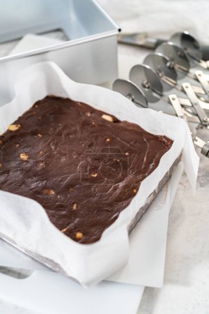 Téléchargez les photos : Enlever le caramel macadamia au chocolat d'un moule à gâteau au fromage carré doublé de parchemin. - en image libre de droit