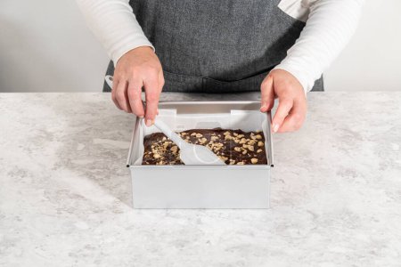 Téléchargez les photos : Poêle à gâteau au fromage carrée garnie de papier sulfurisé avec mélange de caramel pour préparer le caramel aux noisettes au chocolat. - en image libre de droit