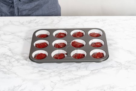 Photo for Scooping cupcake dough with dough scoop into cupcake pan lined with foil liners to bake red velvet cupcakes with white chocolate ganache frosting. - Royalty Free Image