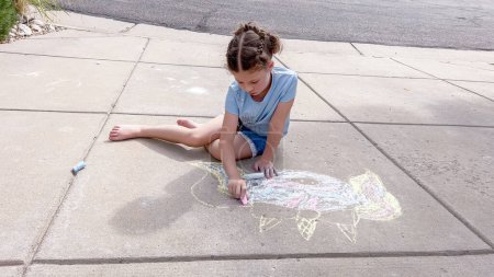 Téléchargez les photos : Petite fille dessinant de l'art crayeux sur une allée de banlieue un jour d'été. - en image libre de droit