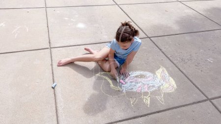 Foto de Niña dibujando tiza en un camino suburbano en un día de verano. - Imagen libre de derechos