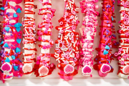 Chocolate-covered pretzel rods decorated with heart-shaped sprinkles for Valentines Day.
