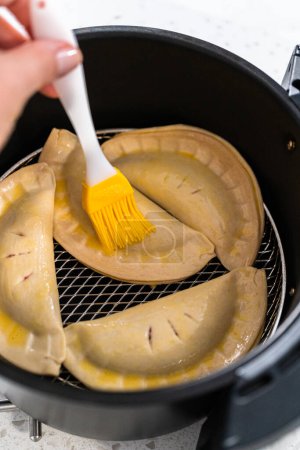 Téléchargez les photos : Brushing uncooked sweet cherry empanadas with egg wash to cook on the air fryer. - en image libre de droit