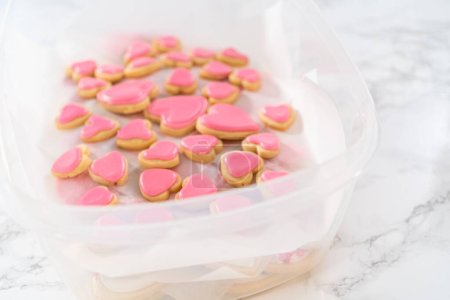 Photo for Storing heart-shaped sugar cookies with pink and white royal icing in a large plastic container. - Royalty Free Image