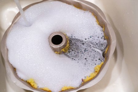 Téléchargez les photos : Plonger dans un moule à gâteau en aluminium sale avec de l'eau savonneuse dans un évier de cuisine. - en image libre de droit