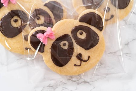 Foto de Embalaje galletas de shortbread en forma de panda con glaseado de chocolate en bolsas claras individuales. - Imagen libre de derechos
