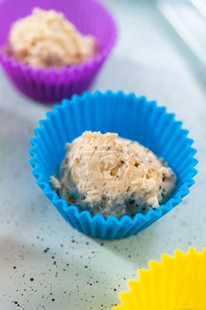 Téléchargez les photos : Cueillette de pâte à cupcake avec cuillère à pâte dans des doublures de muffins de silicium aux muffins de graines de pavot citron. - en image libre de droit