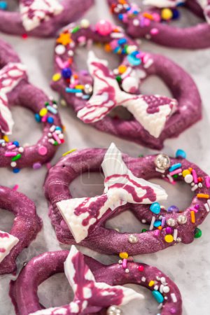 Photo for Homemade chocolate-dipped pretzel twists decorated with colorful sprinkles and chocolate mermaid tails on a white plate. - Royalty Free Image