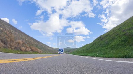 Foto de En un día claro de invierno, un automóvil viaja suavemente a lo largo de la autopista 101 cerca de Santa María, California, bajo un cielo azul brillante, rodeado por una mezcla de vegetación y tonos dorados.. - Imagen libre de derechos