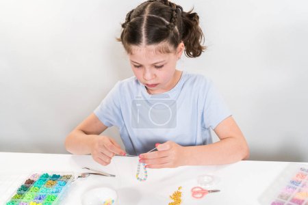 Téléchargez les photos : Petite fille aime confectionner des bracelets colorés avec des perles d'argile vibrantes ensemble. - en image libre de droit