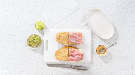 Téléchargez les photos : Pose plate. Assemblage de sandwichs au jambon, concombre et germe sur la planche à découper blanche. - en image libre de droit