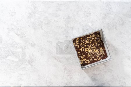 Foto de Acostado. Llenado cuadrado de tarta de queso forrado con papel pergamino con mezcla de caramelo para preparar dulce de avellana de chocolate. - Imagen libre de derechos