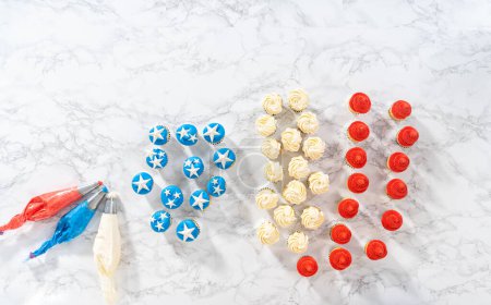 Foto de Acostado. Frosting mini cupcakes de vainilla con glaseado de crema de mantequilla para hacer un mini cupcake de bandera estadounidense. - Imagen libre de derechos