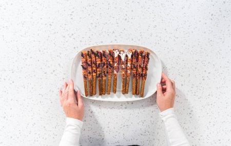 Foto de Acostado. Barras de pretzel cubiertas de chocolate de Halloween con salpicaduras en un plato de servir blanco. - Imagen libre de derechos
