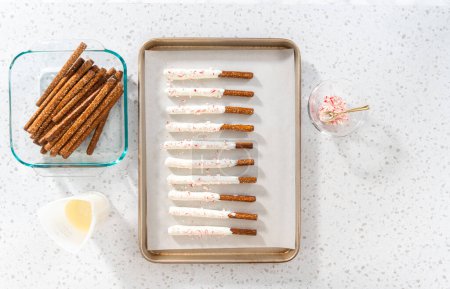 Photo for Flat lay. Dipping pretzel rods into melted chocolate and sprinkling with crushed candy cane candies to make candy cane chocolate-covered pretzel rods. - Royalty Free Image