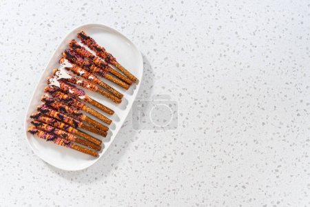 Téléchargez les photos : Pose plate. Baguettes de bretzel recouvertes de chocolat Halloween avec saupoudrer sur une assiette de service blanche. - en image libre de droit